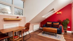 Une pièce chaleureuse de style loft, avec un plafond en pente, une table à manger avec des chaises, un canapé avec des coussins et une grande fenêtre qui laisse entrer la lumière naturelle.
