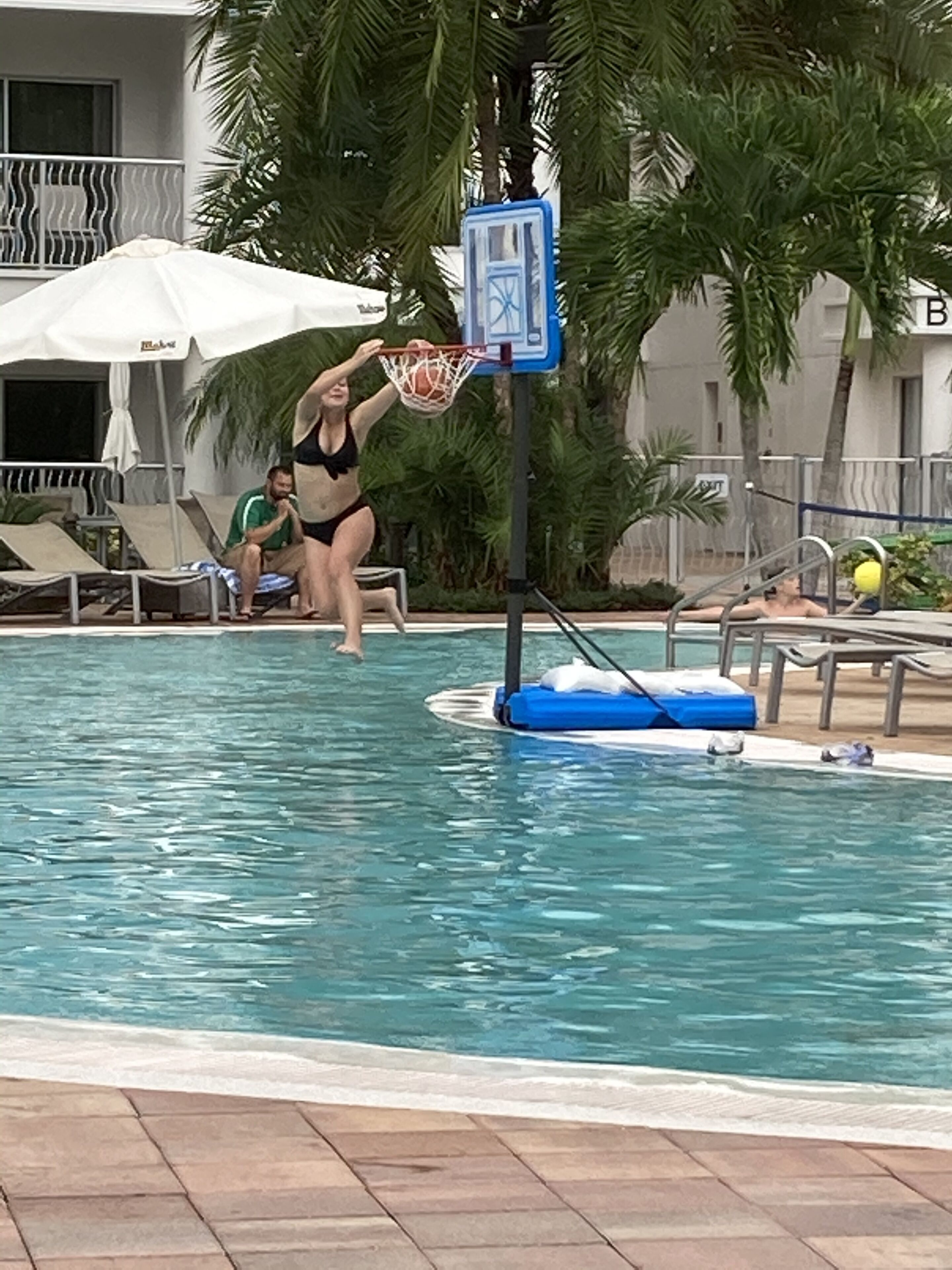 A pool area with lounge chairs, a basketball hoop, and palm trees.
