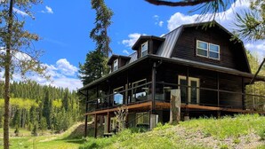 Eine zweigeschossige Holzhütte mit einem Balkon, eingebettet in eine bewaldete Landschaft.