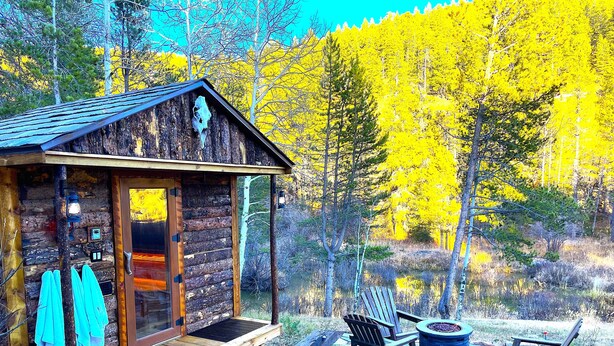 Eine rustikale Holzhütte mit einer Holzterrasse, einem Feuerkorb und Adirondack-Stühlen.