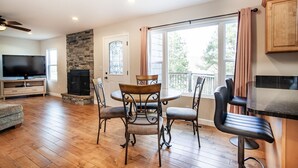 A spacious living area with a fireplace, a dining table with chairs, a television, and a kitchen area with a countertop and cabinets. - Relax on a Scenic Porch Steps from the Historical Trail (Townsend)