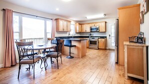 A modern kitchen with wooden cabinets, a central island, and a dining area with four chairs. - Relax on a Scenic Porch Steps from the Historical Trail (Townsend)
