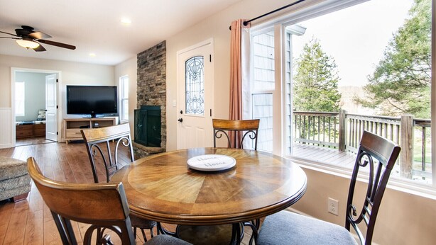 A dining area with a round wooden table, four chairs, a television, and a stone fireplace. - Relax on a Scenic Porch Steps from the Historical Trail (Townsend)
