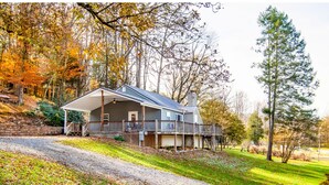 A two-story house with a porch and a covered deck, surrounded by trees and a grassy area. - Relax on a Scenic Porch Steps from the Historical Trail (Townsend)