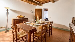 Een eethoek met een houten tafel gedekt voor vier personen, omringd door stoelen, een vloerlamp en een houten kast.