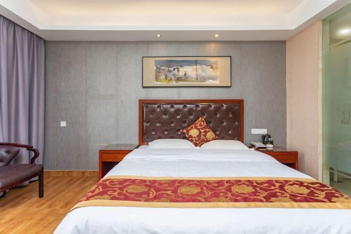 A hotel room with a large bed, a headboard with a tufted design, a wooden nightstand, a chair, and a painting on the wall.