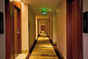 A hotel hallway with doors on both sides, a carpeted floor, and a green exit sign on the ceiling. - Jiabaihe Hotel (Buyong Subway Station Branch) (Shenzhen)