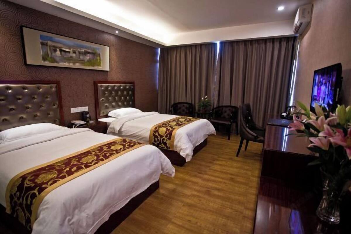 A hotel room with two beds, a desk, a chair, a TV, and a painting on the wall.