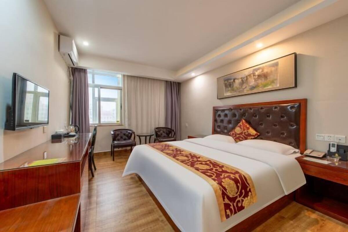 A hotel room with a large bed, a desk, a chair, a television, and a window with curtains.