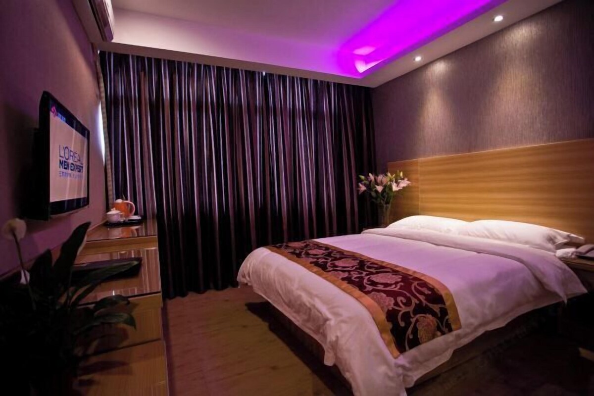 A hotel room with a bed, a nightstand, a TV, and a curtain.