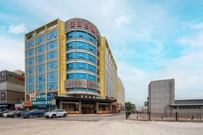 A multi-story hotel with a curved facade, a ground-level entrance, and a parking area with cars. - Jiabaihe Hotel (Buyong Subway Station Branch) (Shenzhen)