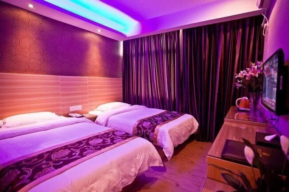 A hotel room with two beds, a wooden nightstand, a television, and a curtain.