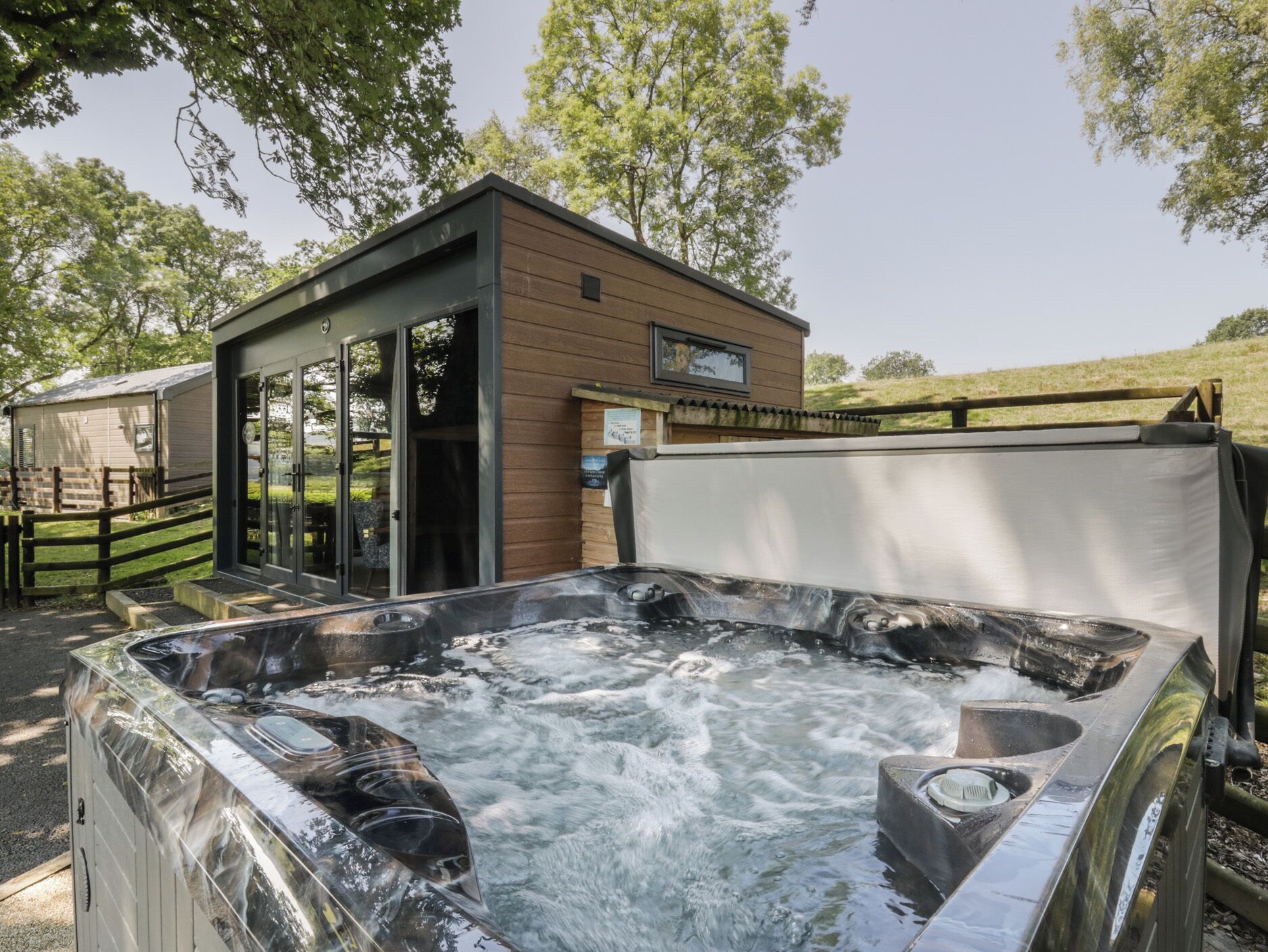 A hot tub with a wooden deck and a small wooden building with glass doors.