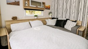 A bedroom with a large bed, a wooden headboard, a TV mounted on the wall, and a window with a view of trees. - Hillside Lodge (Llandrindod Wells)