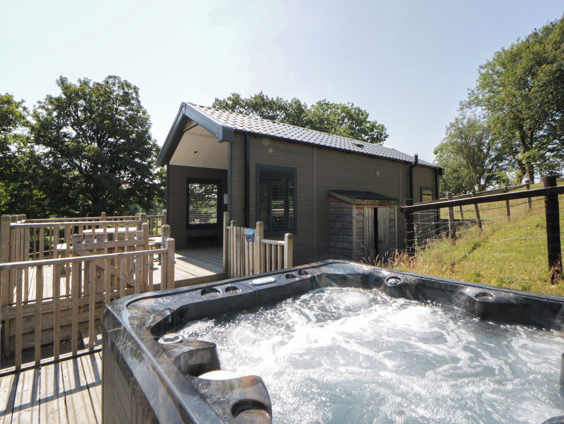 Ein Whirlpool mit einer Holzterrasse und ein Gebäude mit einem geneigten Dach im Hintergrund.