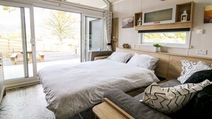 A bedroom with a large bed, a bench, and a TV on the wall. - Hillside Lodge (Llandrindod Wells)