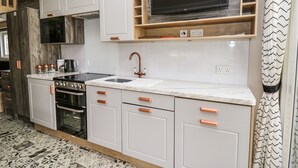 Una cucina moderna con mobili bianchi, una stufa nera, un lavandino e un televisore sopra il bancone.
