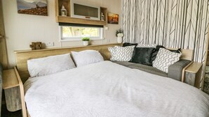 Una camera da letto con un letto grande, una TV montata sopra, un orologio al muro e una finestra vista alberi.
