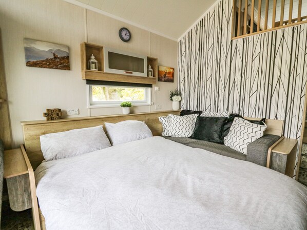 Een slaapkamer met een groot bed, een televisie erboven, een klok aan de muur en een raam met uitzicht op bomen.
