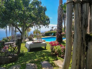 A pool area with a bed, lounge chairs, and a view of the ocean.