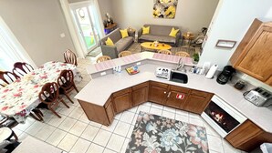 Une cuisine moderne avec un îlot central, un coin repas avec une nappe à motifs floraux et un salon avec un canapé et des coussins.