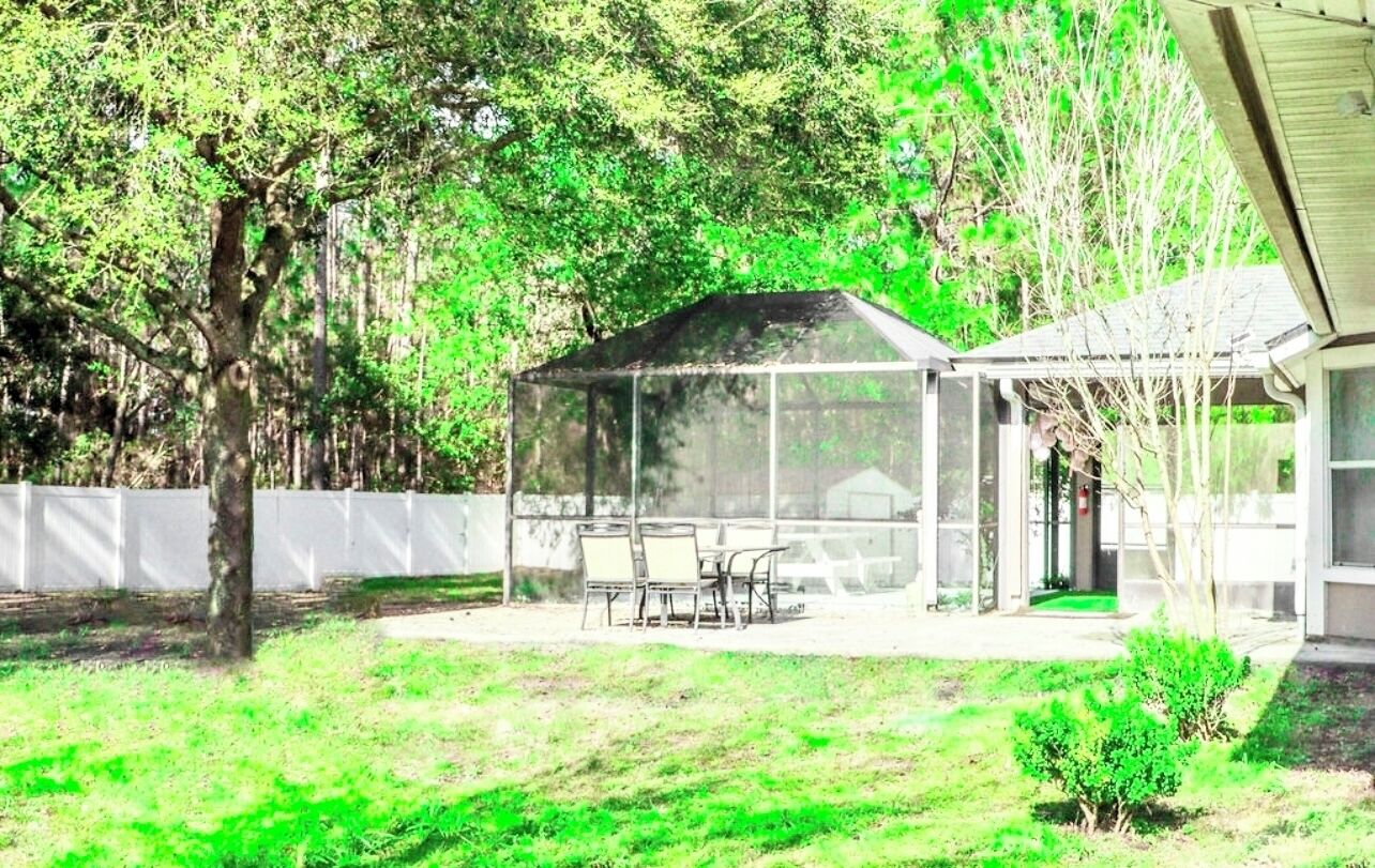 A covered patio with a table and chairs, surrounded by a white fence and trees.