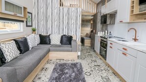Ein modernes Interieur mit einem grauen Ecksofa, einer Küche mit weißen Schränken und Kupferarmaturen sowie einem gemusterten Boden.