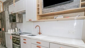 Eine moderne Küche mit weißen Schränken, einer Edelstahl-Spüle, einem eingebauten Ofen und einem Fernseher über der Arbeitsplatte.