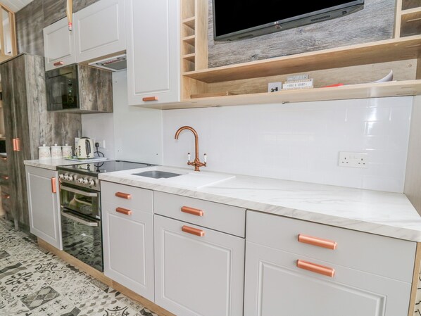 A modern kitchen with white cabinets, a stainless steel sink, a built-in oven, and a television above the countertop. - Hares Rest (Llandrindod Wells)