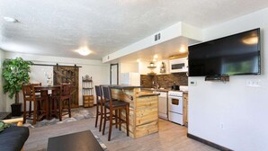 Un espacio habitable compacto con comedor, cocina y televisor fijado a la pared.