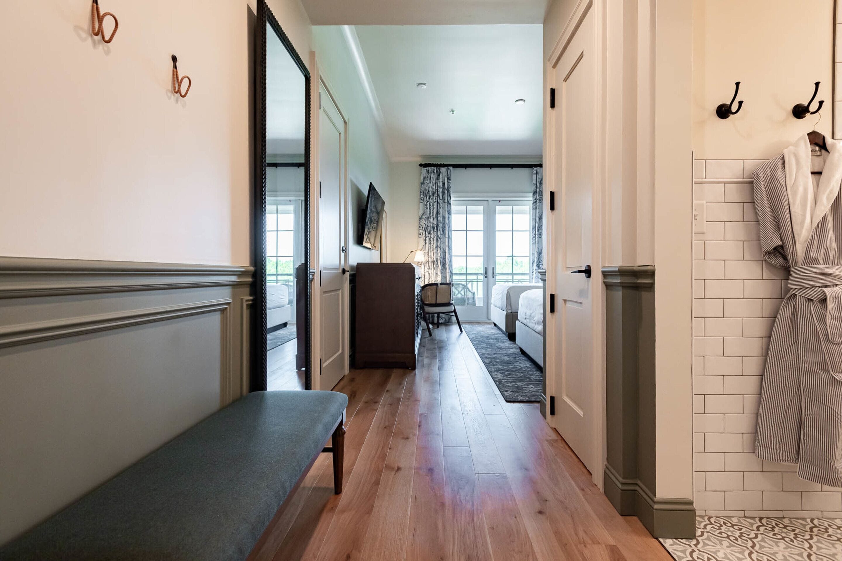 A hallway with a bench, a chair, and a bed in the distance.