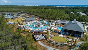 An aerial view of a resort with multiple swimming pools, a large lawn, and a building with a sloped roof. - Camp Creek Inn (Panama City Beach)