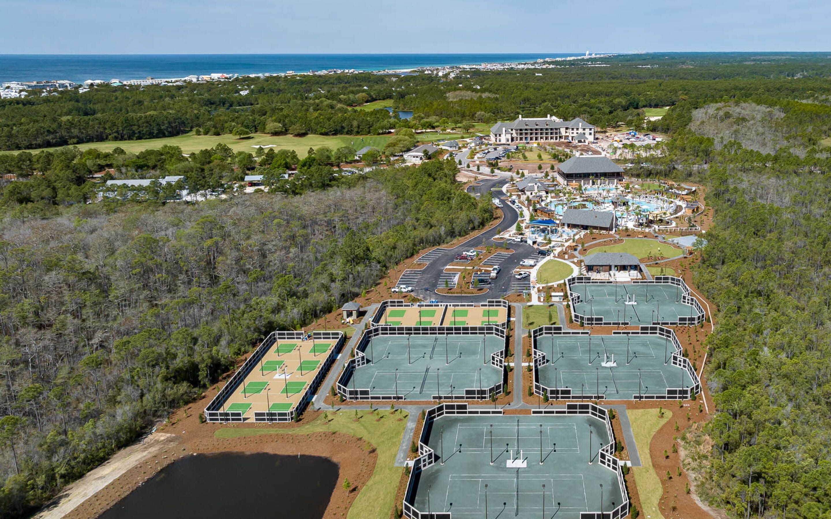 An aerial view of a resort with multiple tennis courts, a large building, and surrounding forested areas.