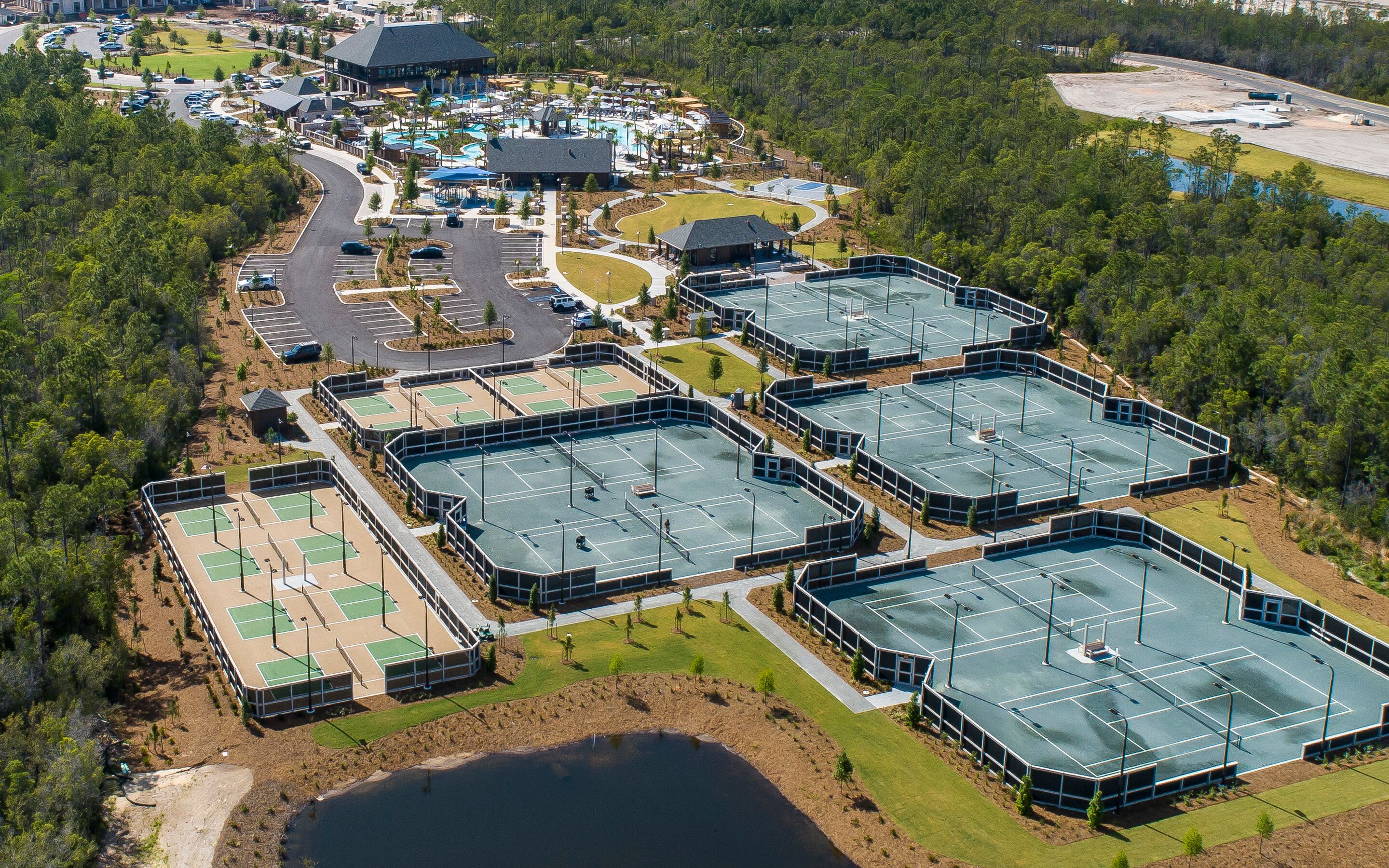 Vista aérea de un complejo turístico con varias canchas de tenis, una piscina y un aparcamiento.