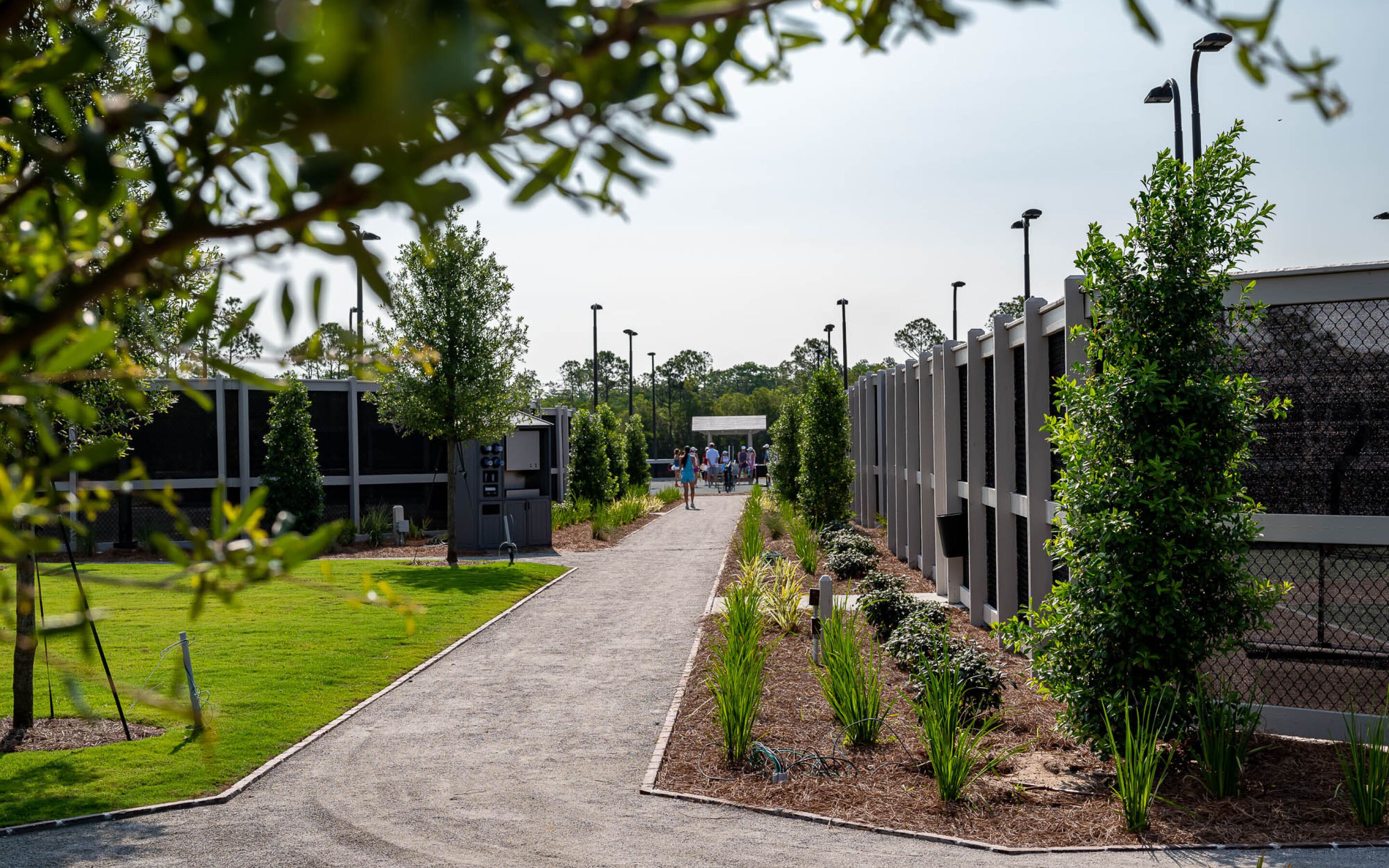 A pathway leading to a building with a modern design, surrounded by greenery and a fence.