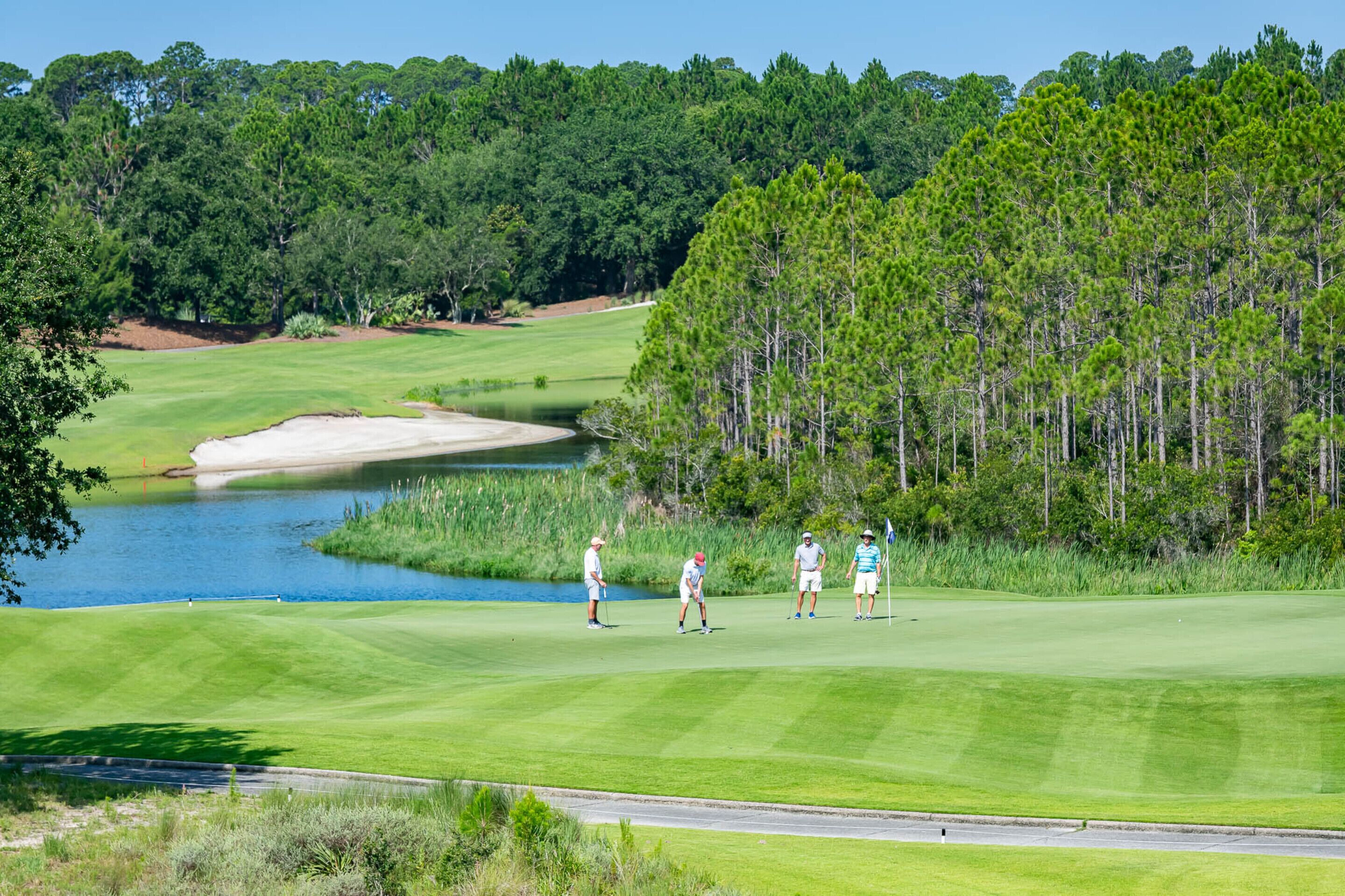 Un campo da golf con uno stagno, bunker di sabbia e alberi fitti sullo sfondo.