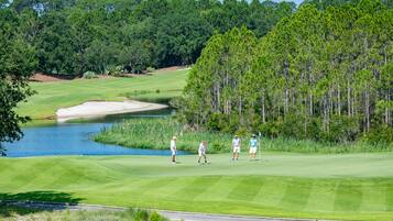 Un campo da golf con uno stagno, bunker di sabbia e alberi fitti sullo sfondo.