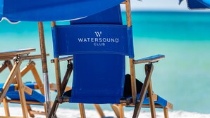 A Watersound Club branded director's chair with a wooden frame and blue fabric, positioned on a beach with a clear view of the ocean. - Camp Creek Inn (Panama City Beach)