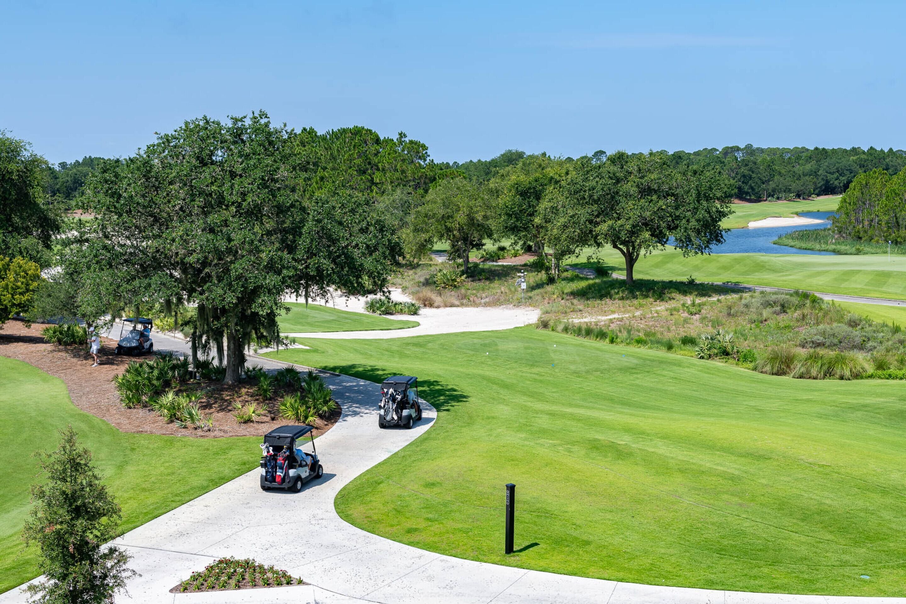 A golf course with a clear path, trees, and a water body in the background.