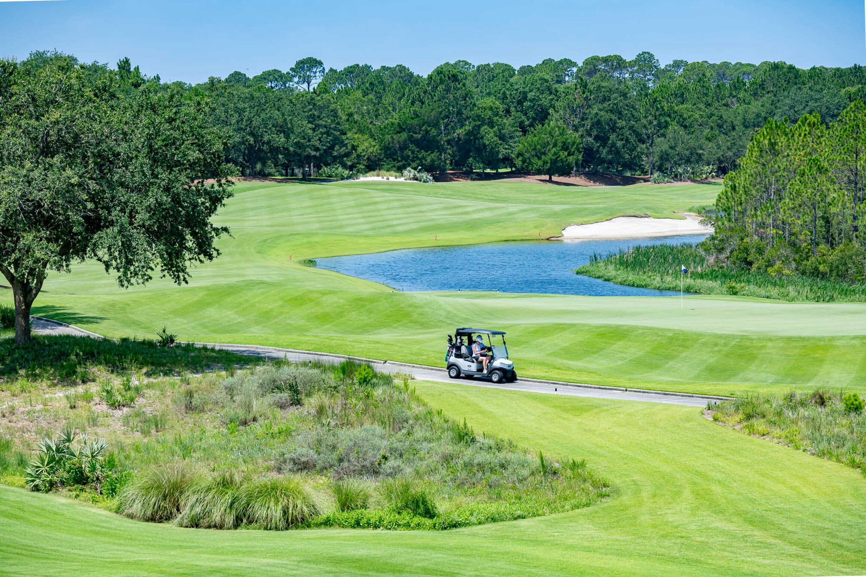 A golf course with a water hazard, sand bunkers, and a golf cart.