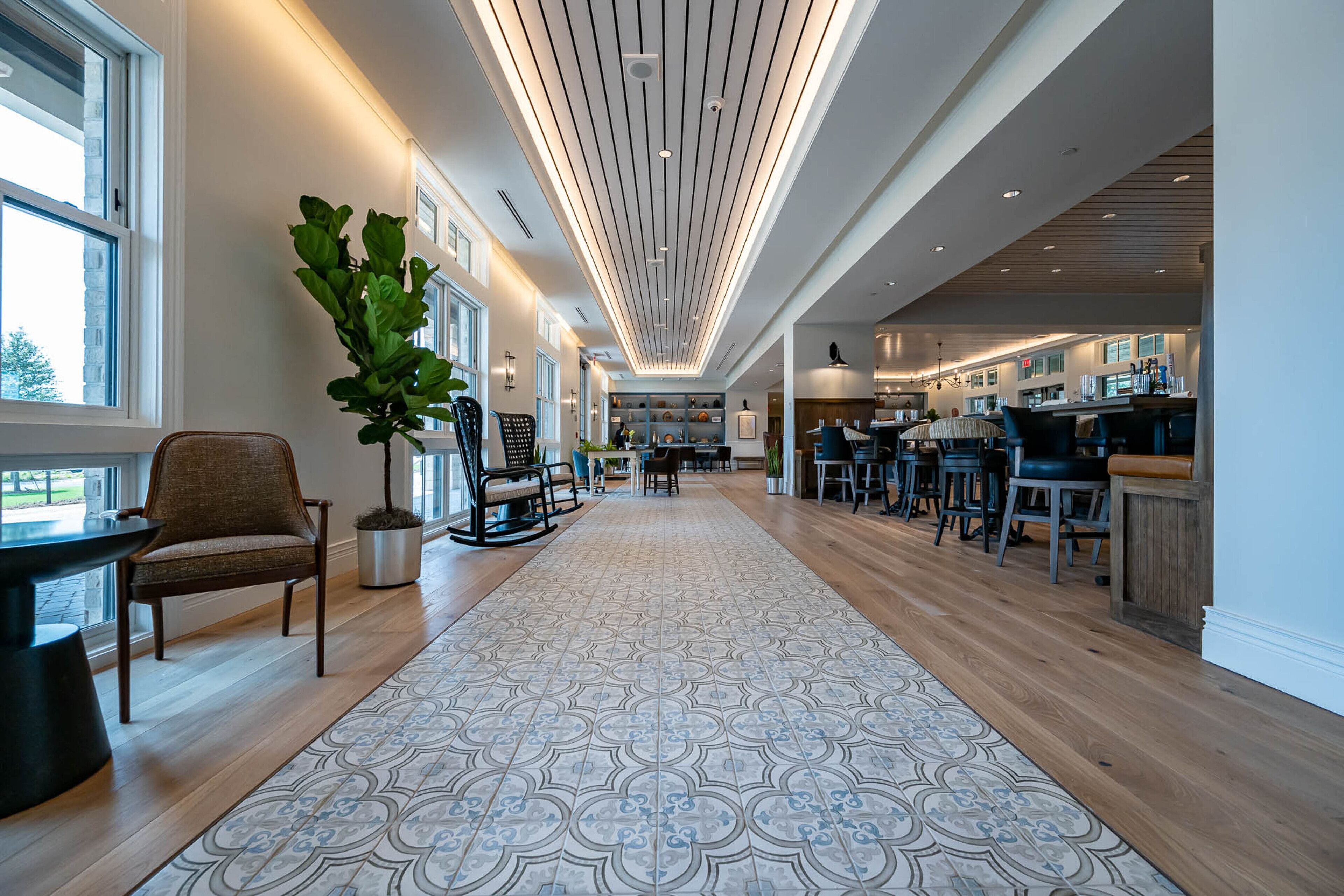 A modern hotel lobby with a patterned carpet, wooden flooring, and a ceiling with linear lighting.