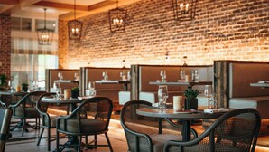 A restaurant with brick walls, round tables, and wicker chairs. - Camp Creek Inn (Panama City Beach)