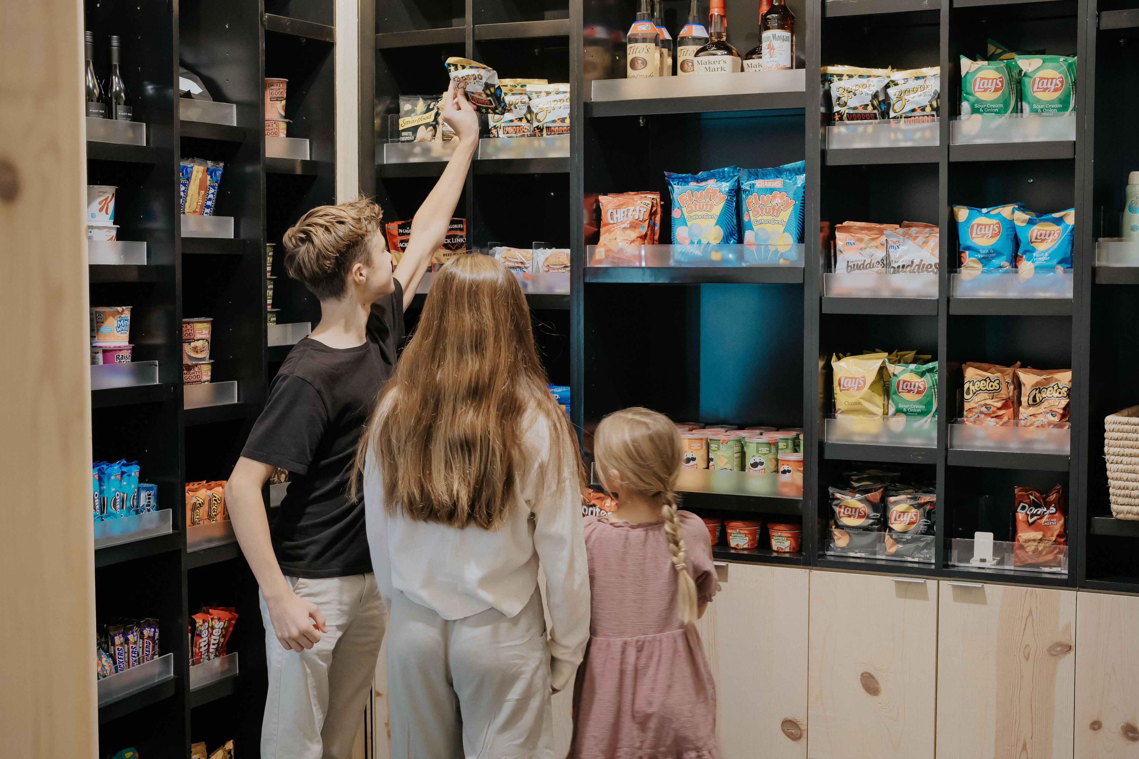 A family selecting snacks from a shelf stocked with various packaged foods.