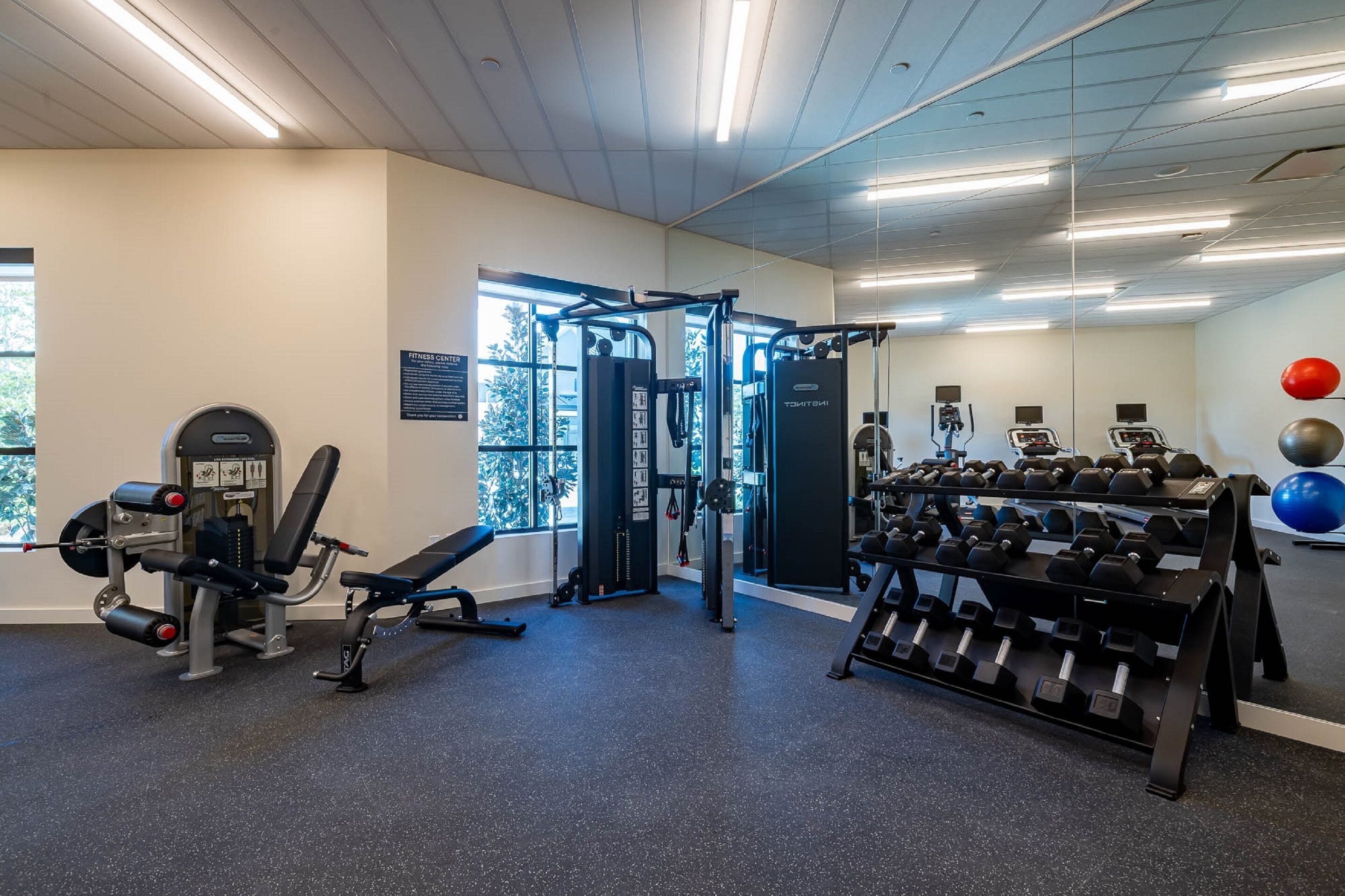 Une salle de sport équipée de machines de musculation, d’un banc, d’haltères et de ballons d’exercice.