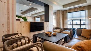 A modern living room with wooden panel walls, a flat-screen TV, a dark coffee table, and leather sofas. - The Lodge 30A (Santa Rosa Beach)