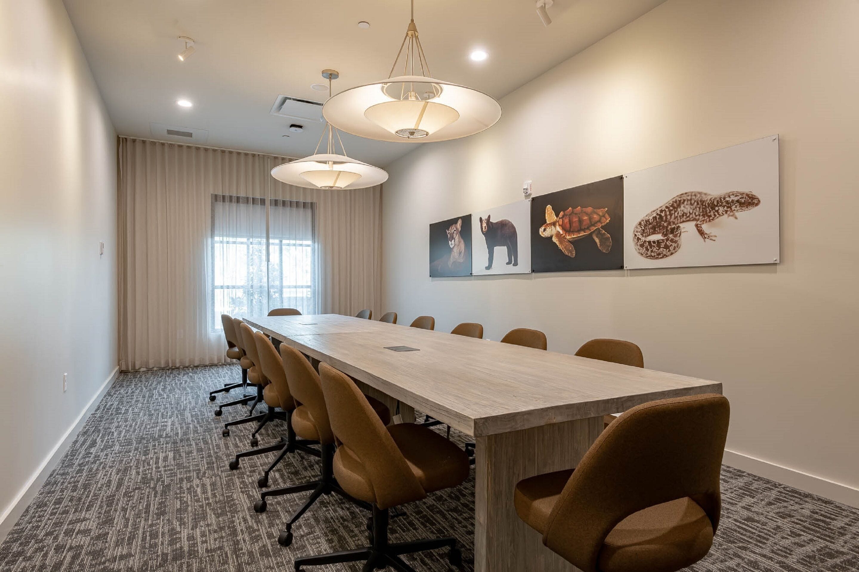A conference room with a long table, brown chairs, and three animal-themed wall art pieces.