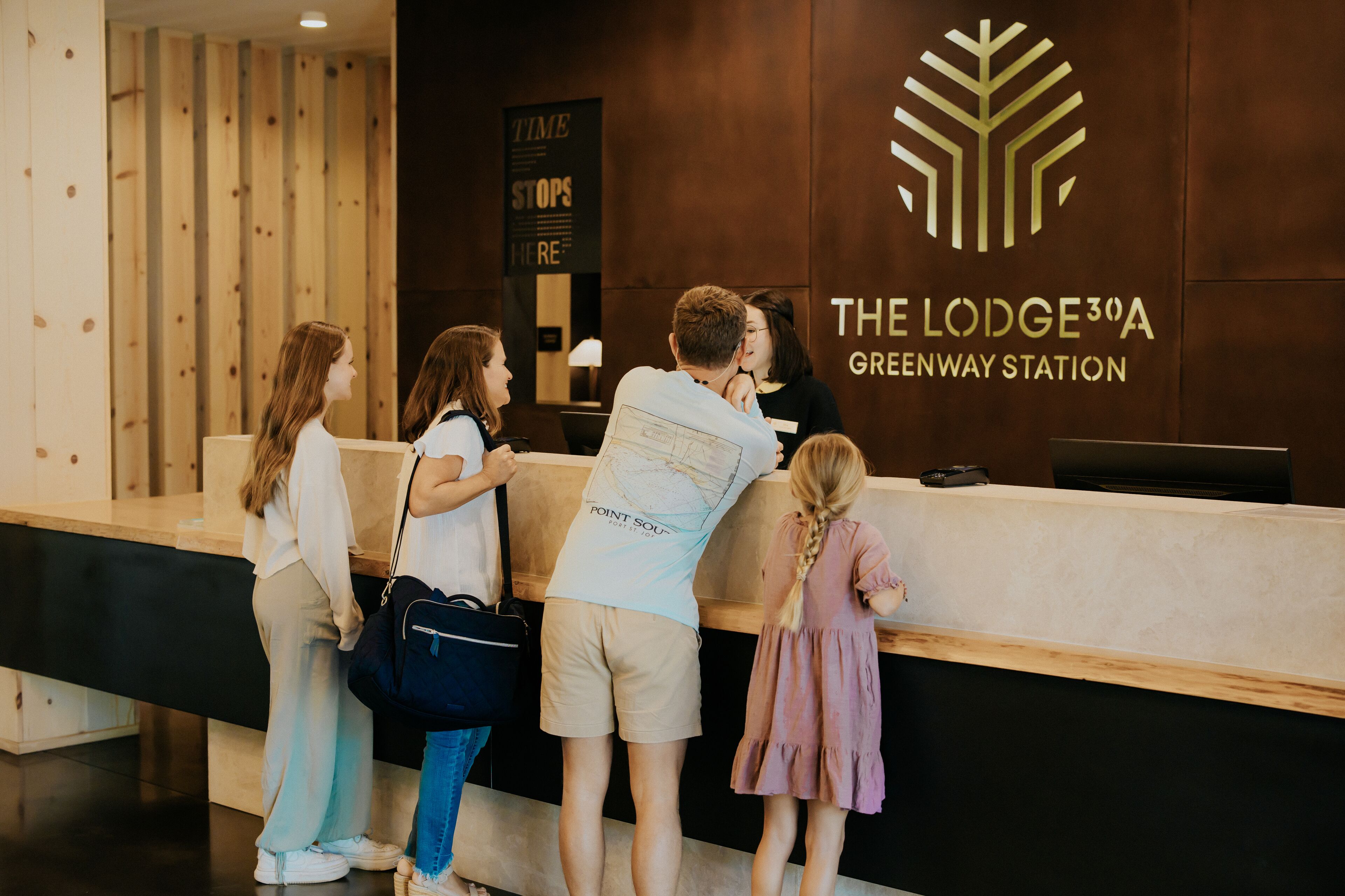 Un comptoir d’accueil à l’hôtel The Lodge 30A Greenway Station, doté d’un design moderne et orné d’un logo sur le mur.