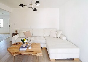 A modern living room with a white sectional sofa, a wooden coffee table with books and a vase of flowers, and a black ceiling light fixture.