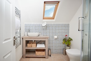 A bathroom with a skylight, a white sink, a wooden vanity, and a potted plant.