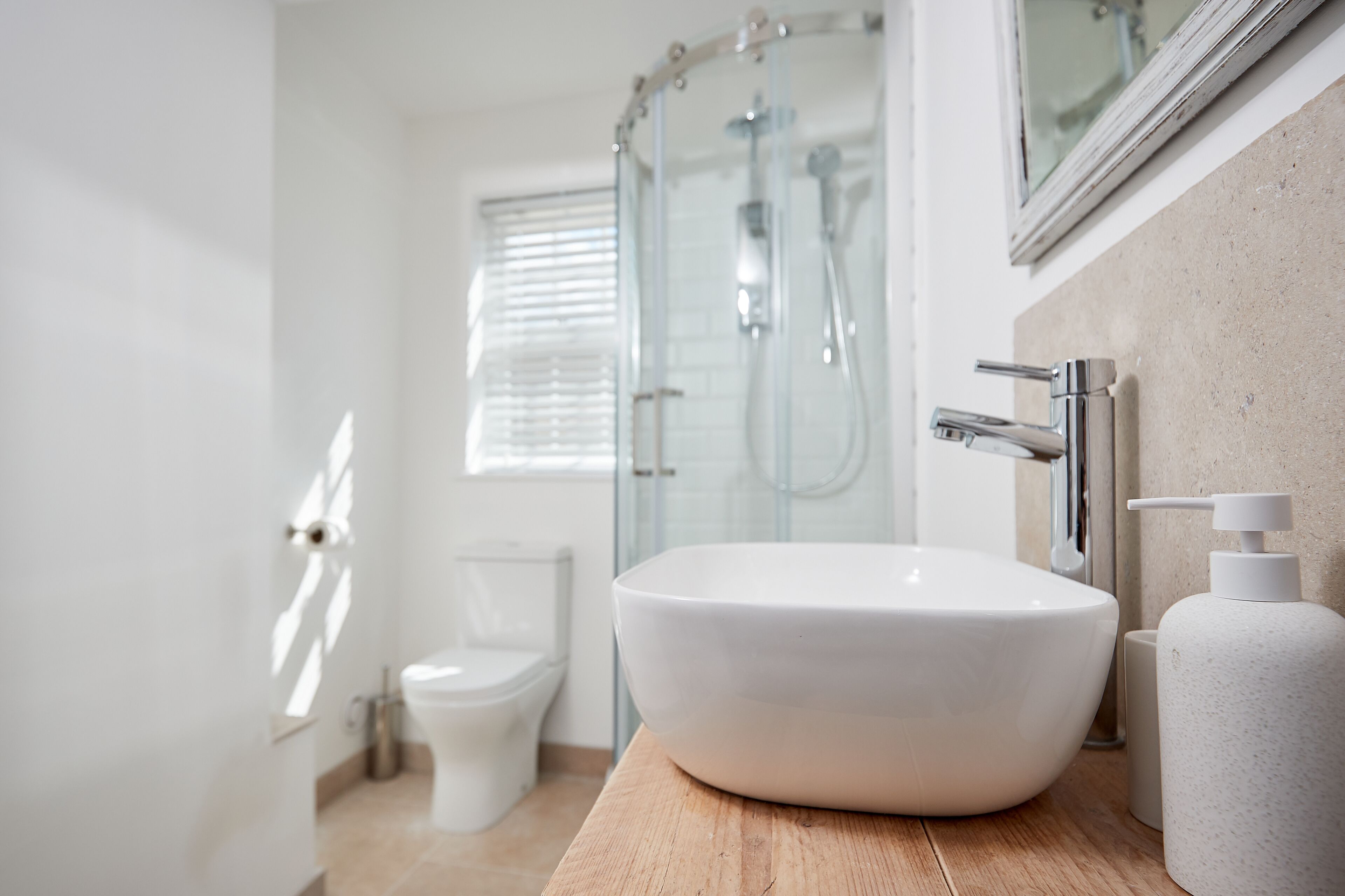 Et moderne badeværelse med en stor, hvid vask, en brusekabine i glas samt et toilet.
